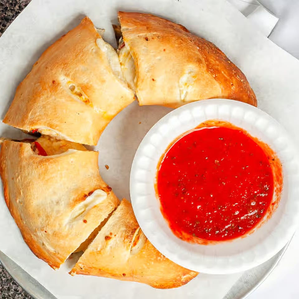 A golden-brown calzone, sliced into four pieces, with a side of red marinara sauce.