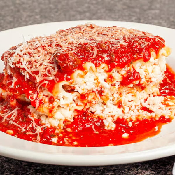 A generous slice of lasagna with rich red sauce, ricotta cheese, and grated Parmesan on a white plate.